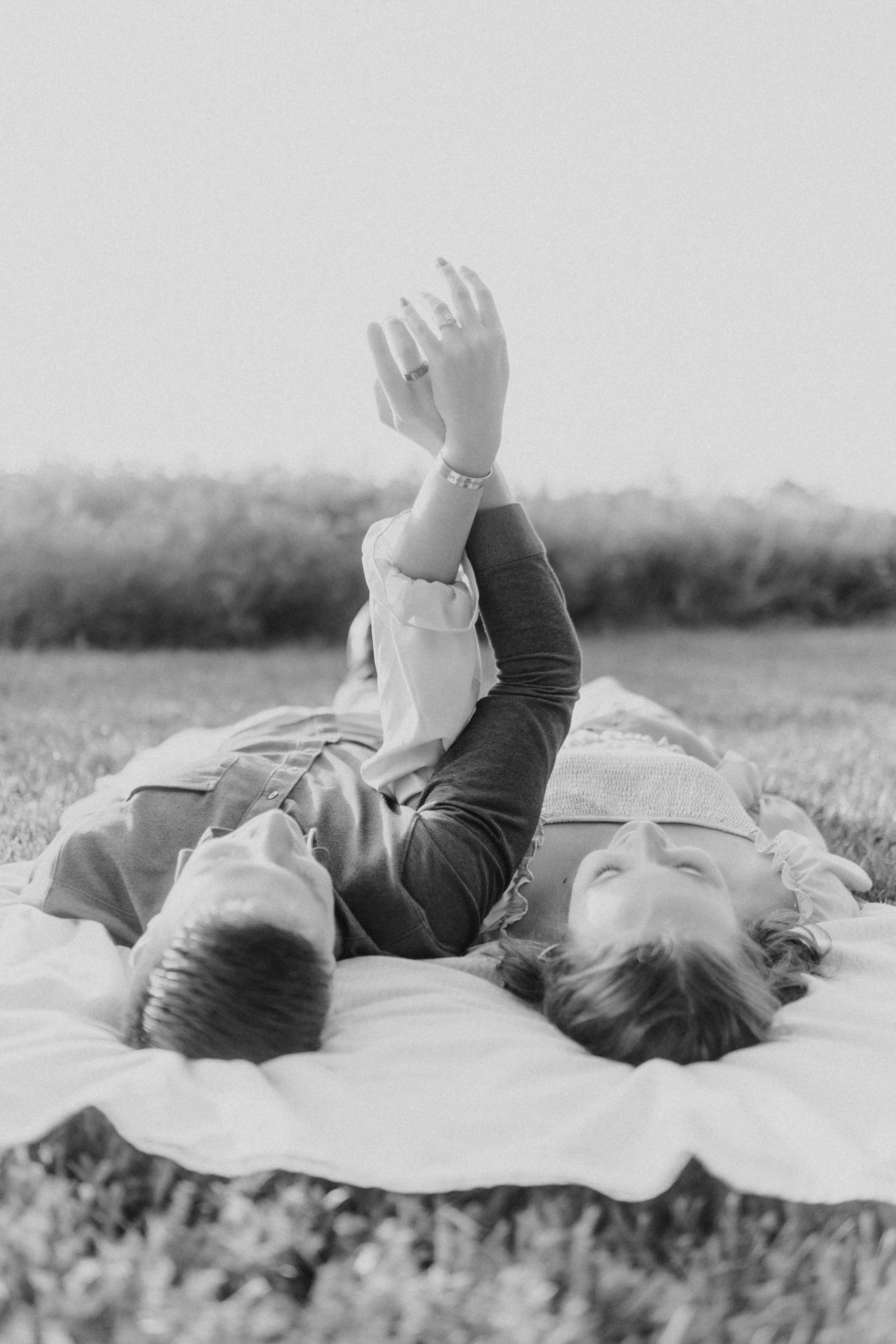 Engagement photo of couple laying on their back with their hands in the sun.